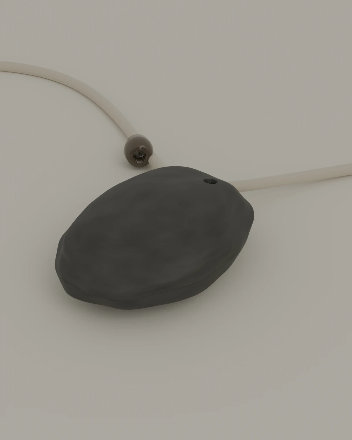 A dark sea-worn stone, drilled once near the top, lying on a pale ground with a waxed cord running through it and off both edges of the frame.