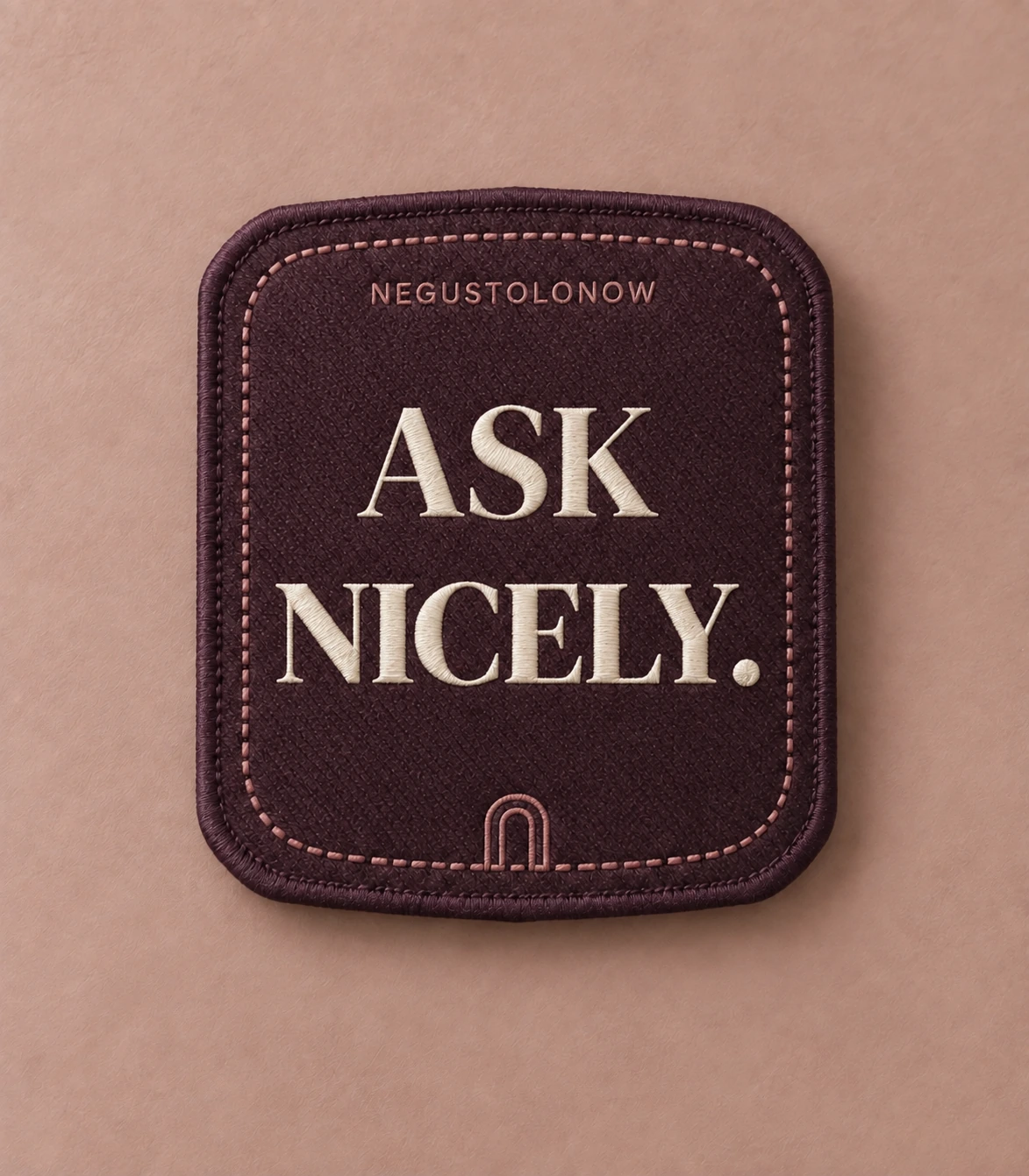 A rectangular aubergine patch with a merrow edge, two words embroidered in ivory, and a small arch stitched below them