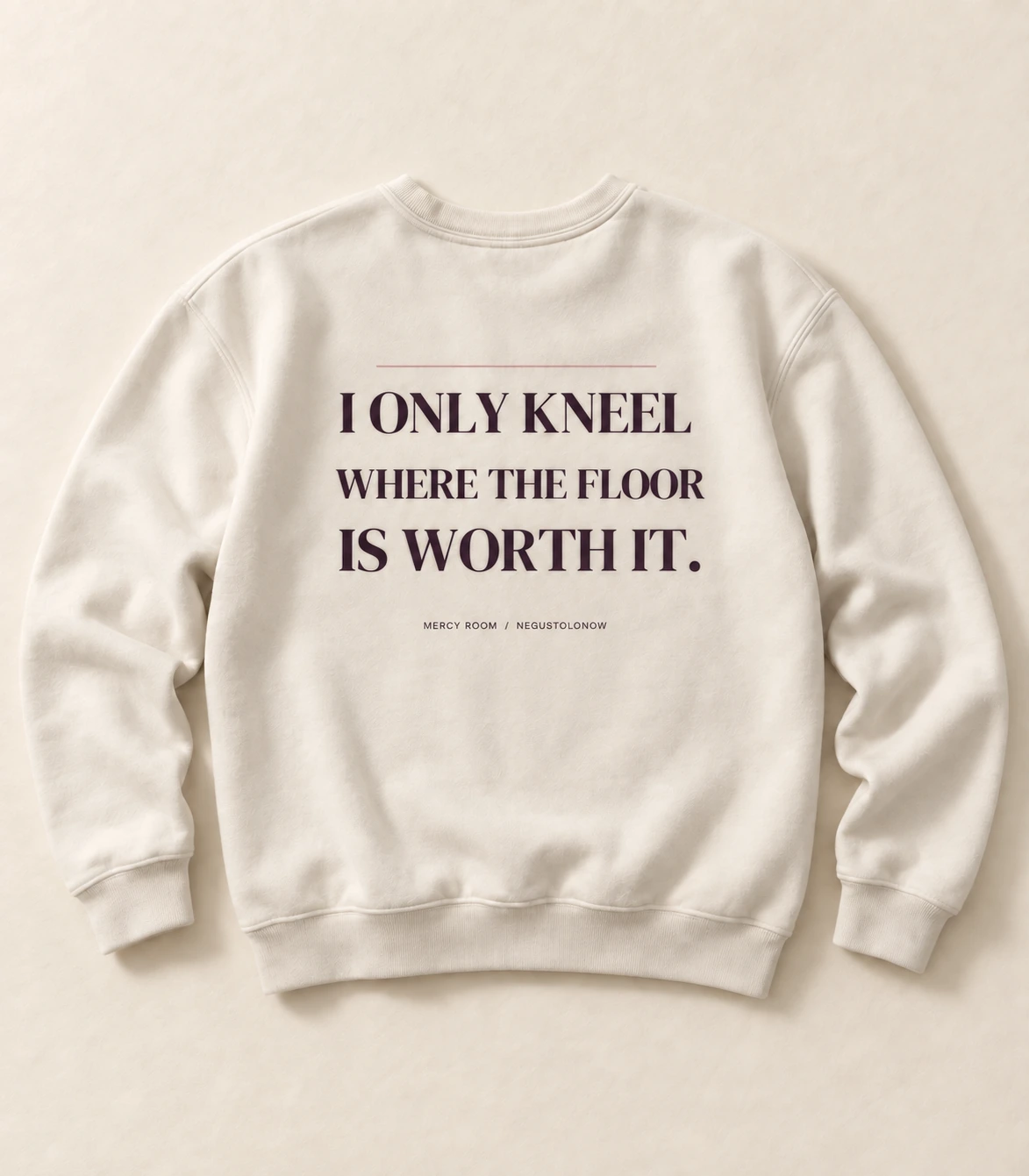 An ivory crew sweatshirt laid flat from behind, one line of type printed across the width of the back in a dark aubergine, with a rule above it and a small mark below.